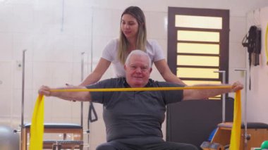 Fizyoterapi seansında kıdemli beyaz adam, Balo ve Elastik Bant Egzersizinde pilates eğitmeninin yardımıyla