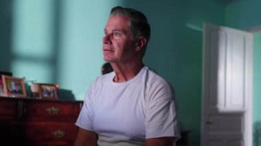 Düşünceli orta yaşlı bir adam yatağının yanında oturup hayatı düşünüyor. Düşüncelere dalmış birinin düşünceli bakışları.