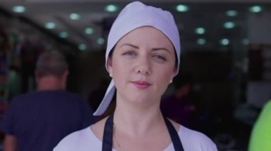 Önlük ve şapka takan, restoran işinin önünde duran kendine güvenen genç bir kadın. Bir kadın sunucunun portresi