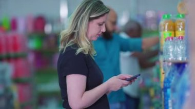 Süpermarket reyonunda cep telefonu ve alışveriş listesi olan bir müşteri.