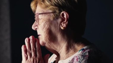 Umut ve İnanç Konsepti: Pencerenin yanında duran, Tanrı 'ya dua eden ve Haç İşaretini Yapan, Katolik Olgun Olgun Bir Kişi Olarak Derinlemesine Adanmış Yaşlı Kadın