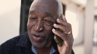 Neşeli Afrikalı Amerikalı son sınıf öğrencisi telefonda gülümseyen, yakın plan çekimde yaşlı siyahi bir insana bakıyor.