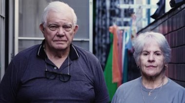 Ciddi bir ifadeyle kameraya bakan yaşlı beyaz bir çiftin dramatik portresi. Grair saçlı yaşlı adam ve kadın