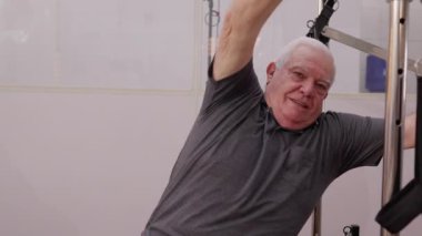 Yaşlı adam pilates makinesiyle vücudunu esnetiyor, yaşlı adam egzersiz yapıyor, yaşlılık egzersizi yapıyor.