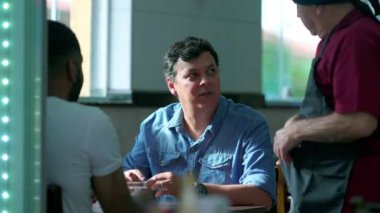 Restoranda oturan garsonla konuşan bir müşteri. Samimi bir Brezilyalı sunucuyla konuşuyor.