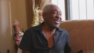 Kanepede oturmuş gülen ve gülümseyen neşeli siyahi bir kıdemli adam mutlu bir Afrikalı Amerikalı 'nın gerçek hayattaki kahkahalarına gülüyordu.