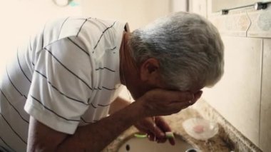 Yaşlı adam sabah rutininde yüzünü yıkıyor. Yaşlı insan güne banyo lavabosuyla başlıyor.