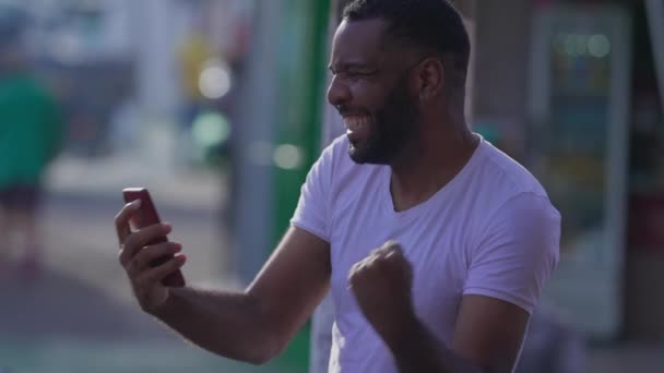 兴高采烈的男人站在城市街道上用手机庆祝好消息 在城市环境中 一个黑人对智能手机上的信息感到高兴 — 图库视频影像