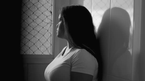 沉思的年轻女子靠在墙上 独自凝视着窗外 20多岁的多愁善感的成年女子独自呆在家里房间里 身披黑白单色戏服 — 图库视频影像