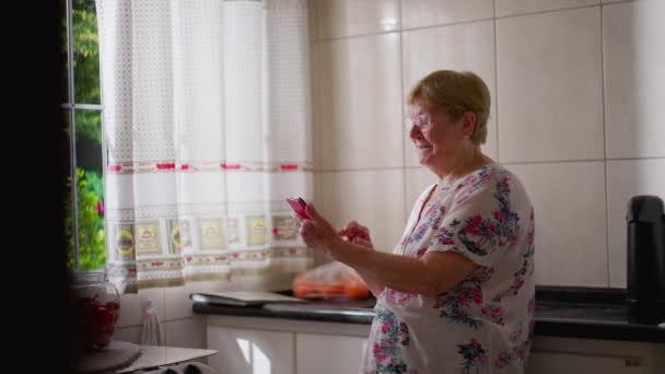 Mujer Mayor Feliz Sosteniendo Teléfono Celular Cocina Del Hogar — Vídeos de Stock