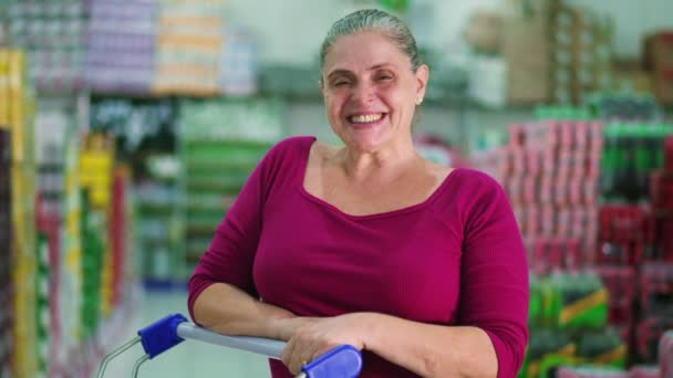 兴高采烈的中年女性消费者站在超市过道里 开着购物车对着相机微笑 — 图库视频影像
