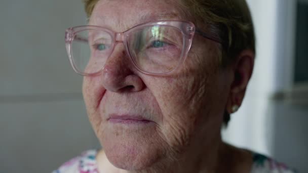 一位老年妇女凝视着窗外的特写 老年人的家庭生活方式独自站在家里 凝视着沉思 — 图库视频影像