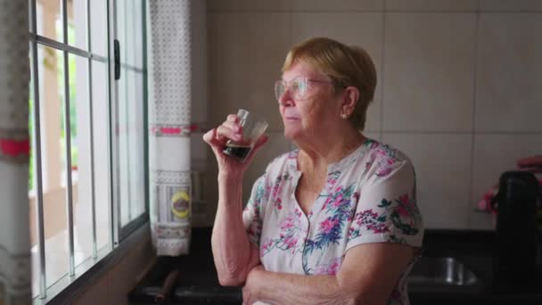 Przemyślana Starsza Kobieta Stoi Przy Oknie Pije Kawę Myśląc Głęboko — Wideo stockowe