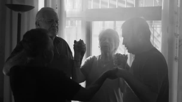 フォギーウィンドウを貫くサンビームと共に モノクロ黒と白に希望を抱くデヴォート グループに囲まれた高齢者個人の祈り — ストック動画