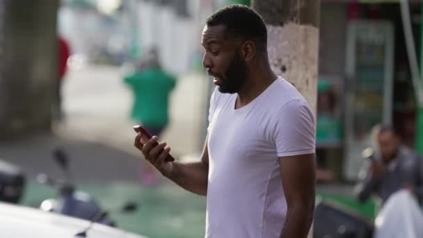 ある黒人男性は 携帯電話機の通知メッセージに対する反応を驚かせた 通りに立って携帯電話を握っているDisbeliefのトップ感情の上にエクスタシーを感じるアフリカ人 — ストック動画