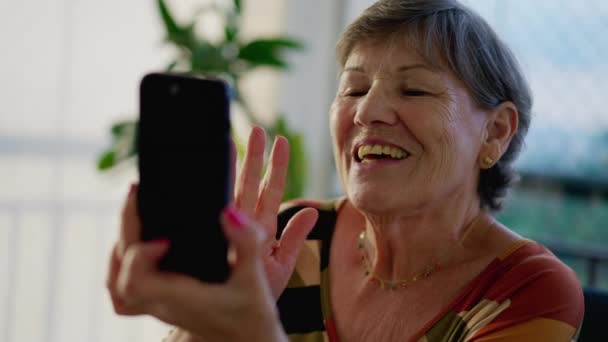 一位快乐的老年祖母的温暖的家庭问候场景向家人挥手致意 在视频交流中拿着带技术屏幕的手机 — 图库视频影像