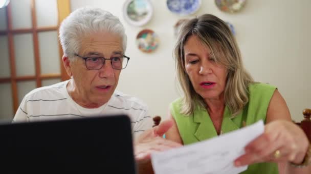 担心的老夫妇盯着笔记本电脑前的财务 手里拿着读书文件 坐在家里厨房里 — 图库视频影像