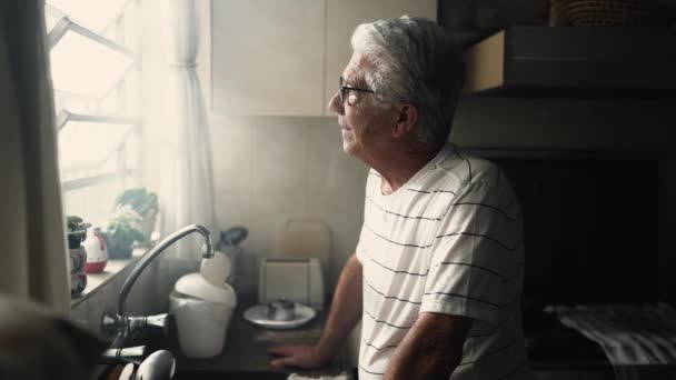 Pensive Senior Man Leaning Kitchen Counter Looking Out Window Thoughtful — Stock video
