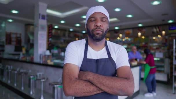 一个年轻而严肃的黑人员工 双臂交叉地站在自助餐厅前面的生意里 — 图库视频影像