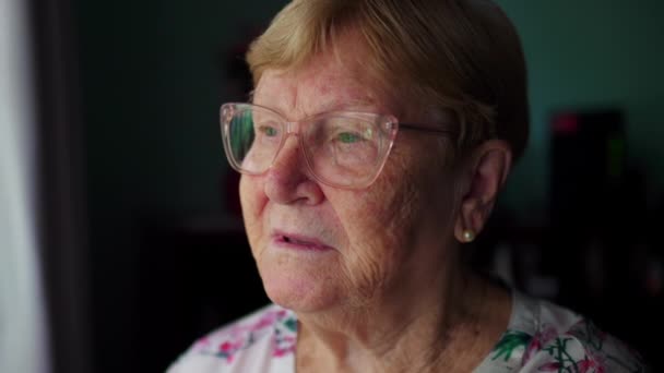 一位年长的老妇人的近视脸 一边凝视着窗外的生活 一边带着沉思的表情 — 图库视频影像