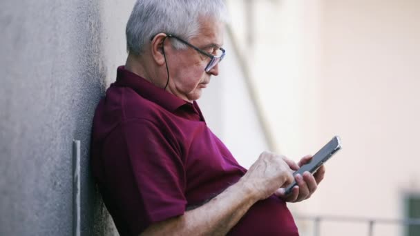 他靠在墙上时 用智能手机装置在外面打人 使用现代技术的真正老年男性高加索人 戴着阅读眼镜 — 图库视频影像