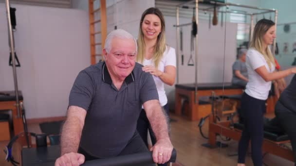 Hombre Mayor Haciendo Ejercicio Pilates Studio Con Ayuda Entrenador Femenino — Vídeos de Stock