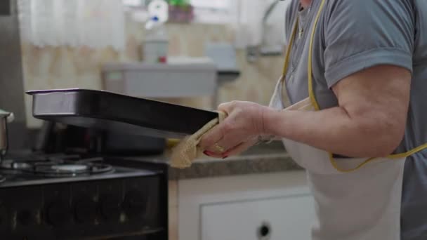 候補者国内高齢者ライフスタイル オーブンから食品を取るシニア女性 キッチンに立っている高齢女性 エプロンと調理食を着用 — ストック動画