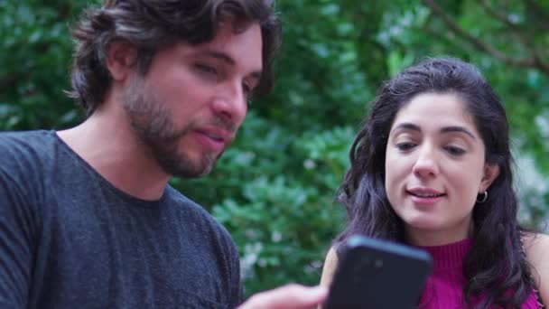 情侣们站在城市公园时 看着智能手机装置 男子和妇女在室外打电话时讨论网上内容 — 图库视频影像