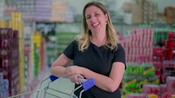 快乐的中年妇女在超级市场购物时 站在过道上笑着 提着推车笑着 — 图库视频影像