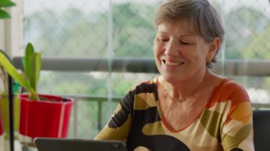 Evde Tablet ile Nişanlı Kıdemli Kadın. Mutlu İfadeli Olgun Yaşlı Kadın Modern Teknoloji Perdesine Bakıyor