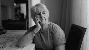 Düşünceli, çenesi içe dönük, boş suratlı, kendinden geçmiş, düşünceli, yaşlı bir kadın.