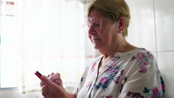 Пожилая Женщина Пользуется Мобильным Телефоном Опираясь Кухонную Раковину Семейный Стиль — стоковое видео