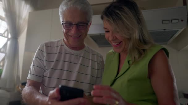 高齢者のデジタル年齢 キッチンセッティングで携帯電話のコンテンツに従事するカップル — ストック動画