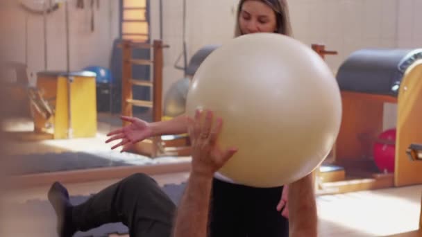 Senior Man Vloer Oefening Met Pilates Ball Onder Vrouwelijke Fysiotherapeut — Stockvideo