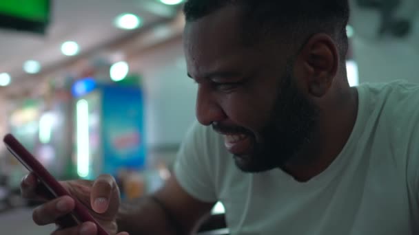 一个快乐的巴西黑人男人坐在餐厅里看着智能手机装置 快乐的人使用现代技术 看着相机 — 图库视频影像
