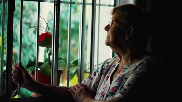 Düşünceli Yaşlı Bir Kadın Evinin Penceresinin Önünde Elinde Barla Dikiliyor — Stok video