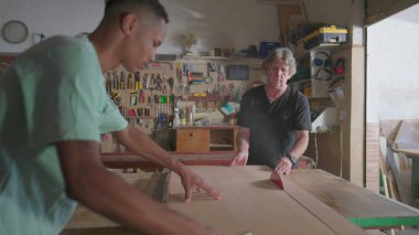 Usta marangoz asistanının yardımıyla testere makinesiyle odun kesiyor. Marangozlukta marangozluk, endüstriyel üretim. Meslek yeri