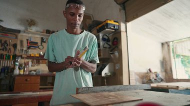 Marangozluk atölyesinde çalışan konsantre olmuş siyah Brezilyalı genç bir marangoz. Tahta kesmeye hazırlanan ahşabı ölçmekle meşgul biri.