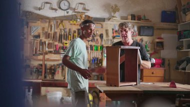 Kıdemli marangoza çırağı, marangozluk sahnesinde ahşap işiyle uğraşan marangozlar yardımcı oluyor.