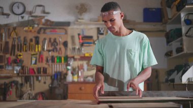 Yoğunlaştırılmış Genç Siyah Brezilyalı Marangoz atölye işiyle meşgul, endüstriyel makineyle odun kesiyor. İş işgali yapan kişi