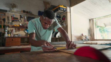 Marangozluk atölyesinde çalışan konsantre olmuş siyah Brezilyalı genç bir marangoz. Tahta kesmeye hazırlanan ahşabı ölçmekle meşgul biri.