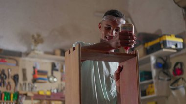 Marangozluk atölyesinde çalışan genç ve mutlu bir marangoz. Çırak işiyle meşgul, nesneyi konsantre ifadeyle yapıştırıyor.