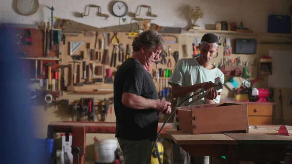 在木工车间工作的高级木匠和初级学徒年轻人的罐头场景 — 图库照片