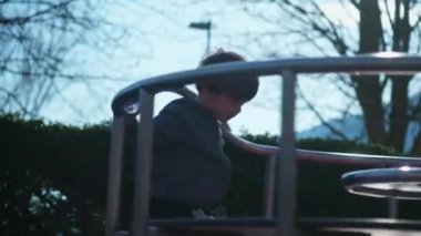 Genç çocuk oyun parkında neşeli bir şekilde oyun oynuyor kaygısız bir şekilde dönüyor, küçük çocuk park çevresinde keyif çatıyor.