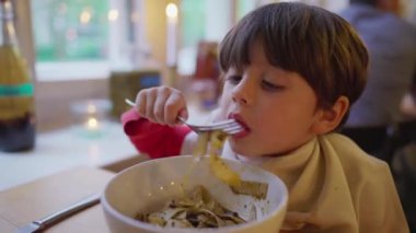 Çocuk spagettiyi kasede yiyor. Aç küçük çocuk restoranda yemeğin tadını çıkarıyor.