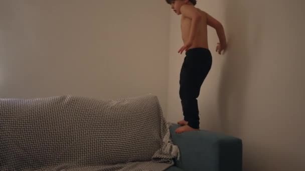 自宅で楽しんでいる子供は ソファーソファの上にジャンプして実行し エネルギッシュなケアフリーの子供 — ストック動画