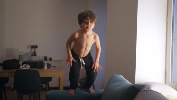 精力充沛 无忧无虑的小男孩在家里跳到沙发上 孩子自己玩乐 — 图库视频影像