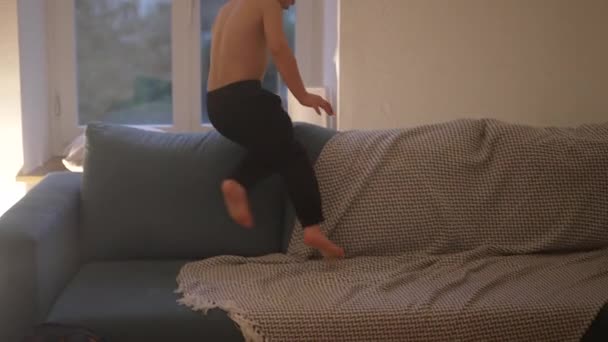 夜のソファーに飛び込む小さな少年 子供は夜に家で屋内遊び 候補者と本物のライフスタイルのシーン — ストック動画