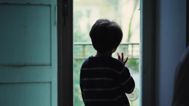 メランコリックの子供が窓のそばに立って ペンギンの悲しい感情を見つめている ガラスに傾いて 内部から眺めている家の星に閉じ込められた小さな男の子 — ストック動画