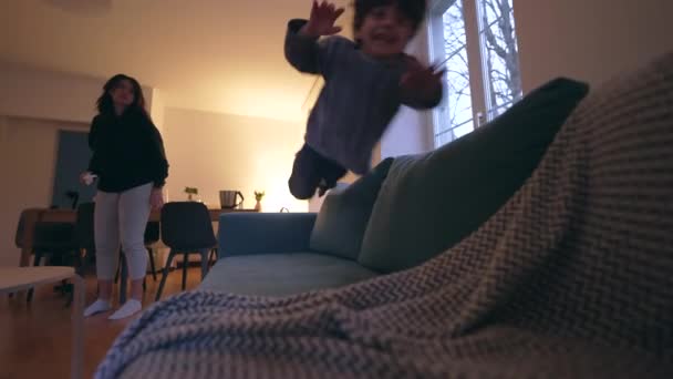 小さな男の子が夜にソファーに飛び込んでいる エネルギッシュなハイパーアクティブな子供が興奮を感じるソファにダイビング — ストック動画